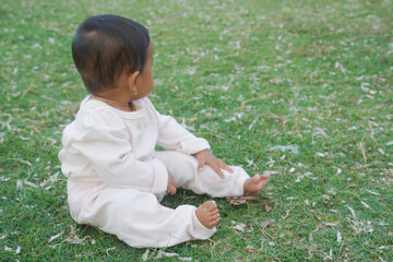 Adorable little baby sitting on green grass outdoors, closeup