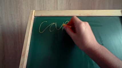 First-person view closeup of a 9-year-old child writing words cat, car, egg, milk, dog, bread on a chalkboard with chalk at home.