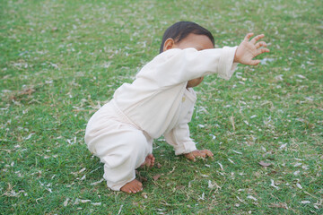 Adorable little baby sitting on green grass outdoors, closeup