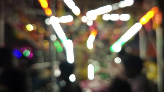Colorful blurred night shot of a big lighted Ferris wheel in an Indian funfair park, with an abstract blurred background of people gathering and shopping at the local city night market.