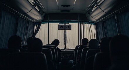 Silhouetted journalists traveling inside a dimly lit media transport bus with a sign on the front window.