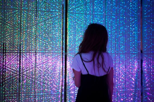 A woman gazing at a mesmerizing display of colorful lights at TeamLab Tokyo, surrounded by a glowing, futuristic ambiance.