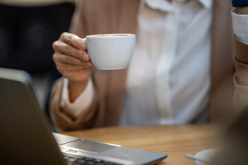 Businesswoman drinking coffee while working on laptop in cafe