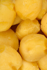 A close-up, high-angle shot shows a dense pile of smooth, golden-yellow peeled boiled potatoes filling the frame