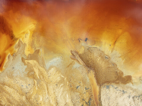 Aerial view of swirling ochre and white waters paint an abstract landscape, reminiscent of desert sands meeting a fiery sky, Minas de Riotinto, Andalusia, Spain.