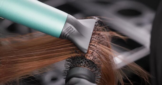 Closeup hair styling with brush and blow dryer, professional salon technique.