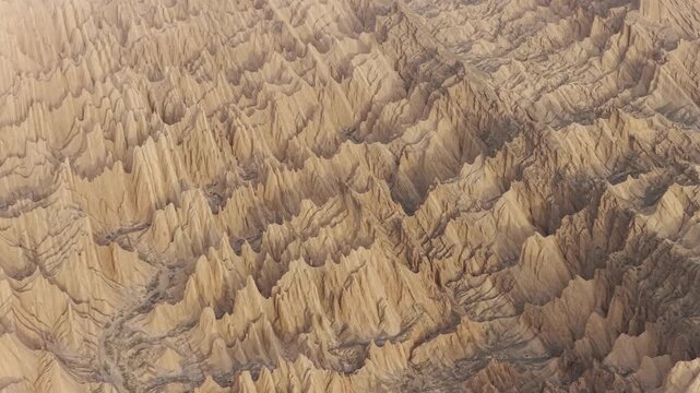 Aerial view of a labyrinth of sun-baked ridges and valleys carve a stark, textured landscape, a symphony of earth tones under the vast sky, Tehran, Iran.