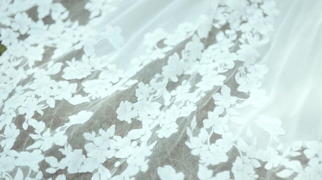 Camera pans low over floral lace wedding train on grass, mesh revealing green