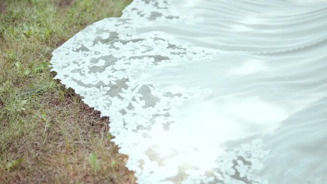 Low pan up shows ornate bridal train on grass, mesh revealing green beneath