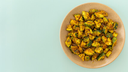 Zucchini Besan Stir Fry. A vegetarian Indian side dish made of zucchini coated with seasoned chickpea flour and stir-fried. Light peppermint color background with space for text or logo.