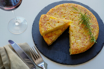A sliced homemade Spanish omelette (tortilla de patatas)  placed on a black plate and a glass of red wine 