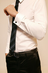Man in a white shirt with a tie and black pants, adjusting his cufflink.