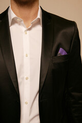 Man in a black suit with a white shirt and a purple pocket square.