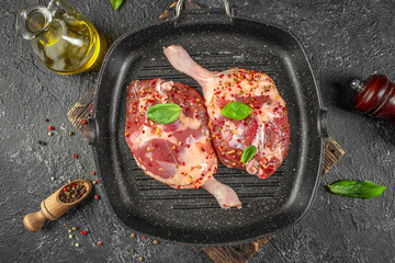 Raw duck legs seasoned with herbs and pepper in a grill pan, ready for traditional confit preparation. top view