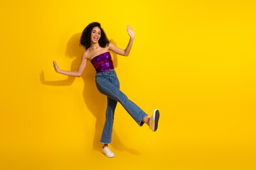 Young woman dances in purple sequin top jeans on bright yellow backdrop expressing joy and confident style