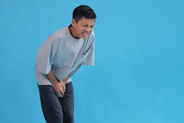 Young Asian Boy Covering His Crotch Suffering from Genital Organ Problem Isolated on Blue Backdrop © Gatot
