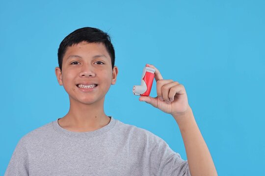 Smiling Asian Boy Showing Asthma Inhaler Against Vibrant Blue Background for Healthcare Awareness