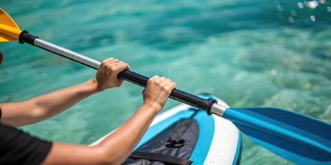 Hands holding inflatable kayak paddle on clear water with blurred background showing outdoor activity