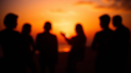 Blurred silhouettes of a group of people standing against a bright orange sunset over the sea or horizon. An atmosphere of friendship and tranquility