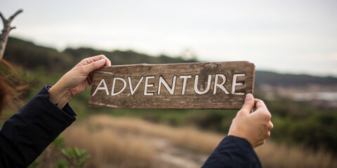 Adventure travel concept with wooden sign held by person outdoors in natural landscape inspiring exploration and journey