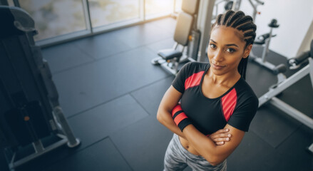 Obraz premium Confident athletic woman with arms crossed in a modern gym. Portrait of a strong female after a workout. Health and fitness lifestyle concept