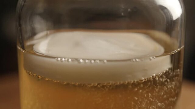 A white SCOBY pellicle, a symbiotic culture of bacteria and yeast, ferments sweet tea in a glass jar.