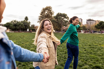 Cheerful multiracial female friends holding hands, leading and following, enjoying time together in a city park