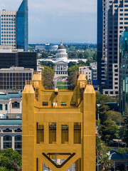 Aerial view of Sacramento, California, featuring the golden Tower Bridge, the State Capitol Building, lush greenery, and modern high rise buildings. © Aerial Film Studio