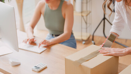 Close Up Of Two Women Running Online Fashion Business From Home Sealing Order In Box