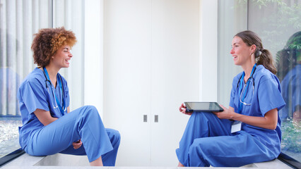 Obraz premium Two Female Doctors Wearing Scrubs With Digital Tablet On Break In Hospital Talking Together