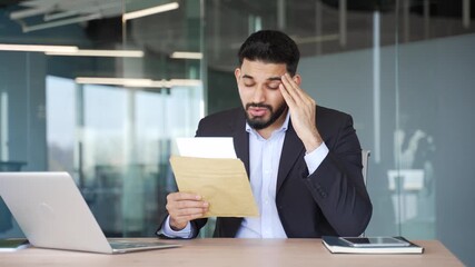 Worried businessman reading letter with bad news while sitting at desk at workplace in business office. Disappointed upset entrepreneur in formal suit frustrated by received negative notification - Powered by Adobe