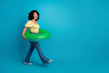 Young woman in vibrant attire holding a green inflatable ring against a blue background, radiating joy and summer vibes