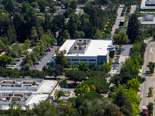 Aerial view of a modern office building with a flat roof, parking lots, and lush greenery in...