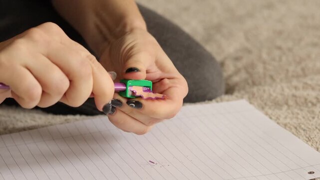 A person demonstrates sharpening a purple pencil using a green sharpener on a sheet of paper. The focus is on the neat results of this essential writing tool
