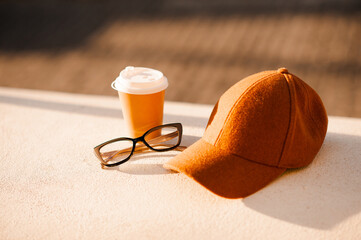 Cup of coffee with eye glasses and cap in sun light outdoors close up. Autumn lifestyle concept.