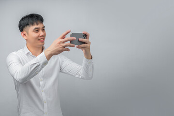 A handsome young Asian man smiles happily while using a social media or gaming app on a modern smartphone. This concept is ideal for technology, connectivity, lifestyle, and leisure.

