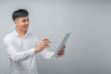 A handsome young Asian man looks pleasantly surprised while reviewing a document or financial statement. This concept is ideal for business, finance, investment, technology, and advertisement.