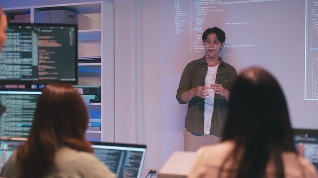 Asian man presents code during a software development meeting or coding workshop, guiding attendees through problem-solving and programming concepts in an educational setting.