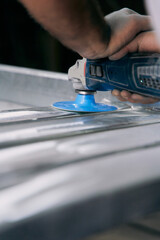 Close up of workers hand operating an angle grinder with blue disc to polish and smooth metal surface in industrial workshop.