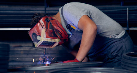 Obraz premium Skilled factory worker welding metal parts while wearing protective mask, gloves, and safety gear in an industrial workshop with sparks flying.