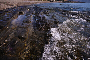 Sea waves crash against the coastal ridge of flat rock formations on the shore.