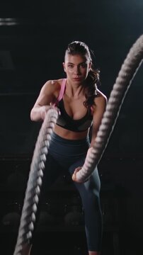 Athletic woman training with battle ropes in gym front view confidence focus discipline healthy lifestyle motivation strength endurance concept slow motion fitness vertical video