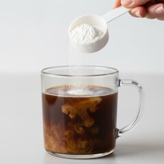 Hand adding collagen powder supplement to coffee in a glass mug.
