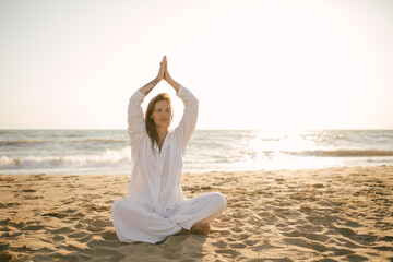 Beautiful 40 years old woman having yoga exercises on th beach at sunset.