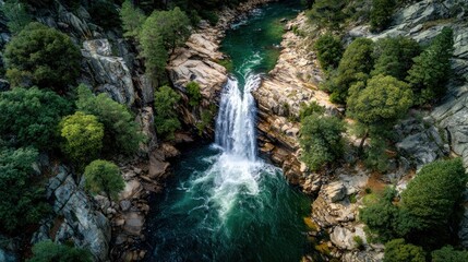 Breathtaking aerial view of powerful cascading waterfall flowing into a turquoise river surrounded by lush green forest and rugged rocky cliffs in a nature landscape
