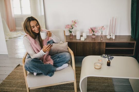 Young woman using her smartphone, relaxing in a cozy living room.