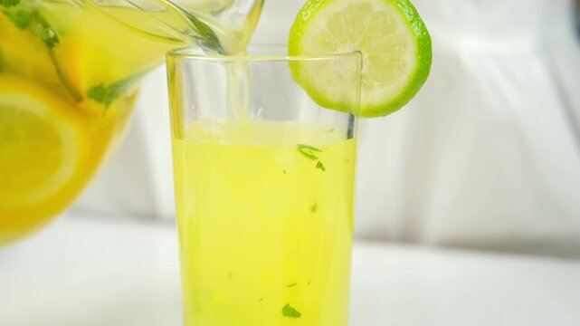 Woman pouring homemade lemonade from citrus fruit herbs in glass with ice. Cooking fresh organic beverage with herb mint orange lime lemon on kitchen at home. Recipe cuisine culinary ingredient.