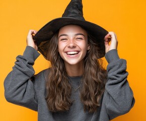 A joyful young woman, adorned with a witch's hat, beams with a wide smile against a vibrant yellow backdrop.