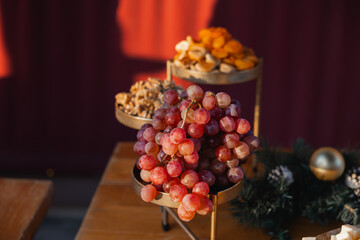 Close-up of fresh red grapes on a tiered serving stand with dried fruits and nuts in the background, perfect for festive gatherings