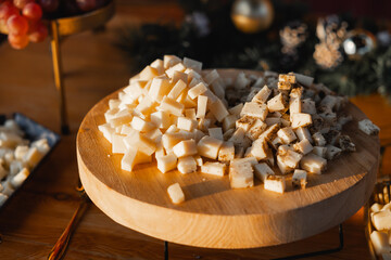 Close-up of cubed plain and herb-seasoned cheese served on a round wooden board, ideal for catering, parties, or wine pairing